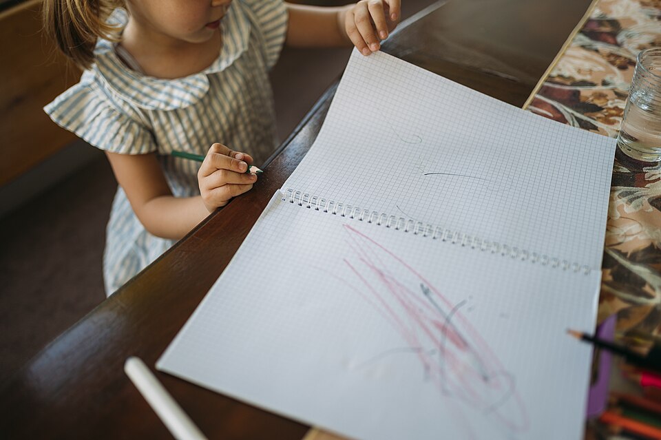 Criança desenhando com lápis de cor em um caderno durante atividade lúdica